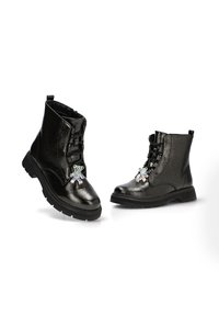 Botas de tobillo de cuero negro con un acabado brillante, que cuentan con un diseño de cordones, un charm de oso de peluche en el frente y una suela de goma resistente.