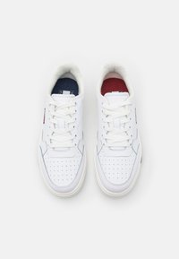 Białe sneakersy z gładkiej skórzanej cholewki, perforowanym noskiem i kontrastowym czerwono-niebieskim wykończeniem. Posiadają białe sznurowadła i wyściełany kołnierz.