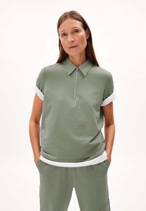 Polo shirt in muted green fabric with a short zip and folded white cuffs. Paired with matching green pants featuring a white waistband.