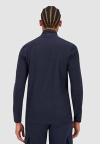 Top a maniche lunghe blu navy realizzato in tessuto morbido, con un colletto alto e una vestibilità dritta. Texture liscia senza motivi o accenti visibili.