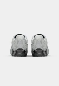 Gray athletic shoes with mesh and synthetic materials, designed with curved accents and a black outsole. Back view shows padded collars.