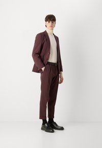 Maroon suit jacket and matching trousers with a fitted cream turtleneck. Black belt and shoes complete the look. Minimalistic design and tailored fit.