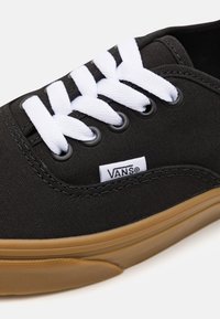 Svart Vans-sneaker med vita snören, gummisula och synlig Vans tyglogg vid snörena.