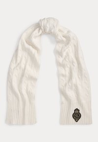 Bele ruta z vzorcem pletenja in rebrastimi konci ter z logotipom, ki prikazuje krono in začetnice. Mehka tekstura in srednje dolžine.