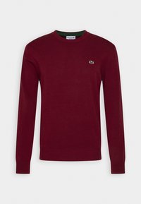 Bordeauxfärgad tröja i stickad kvalitet, med rund halsringning och långa ärmar, samt en grön krage och en liten logotyp på bröstet.