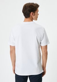 Camiseta de algodón blanca vista desde la parte de atrás, con cuello redondo, mangas cortas y un dobladillo recto con una textura suave.