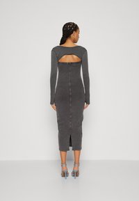Robe midi grise à côtes avec manches longues et détail en découpes dans le dos. Présente une fente arrière, une coupe ajustée et un tissu texturé. Accompagnée de talons bleus.