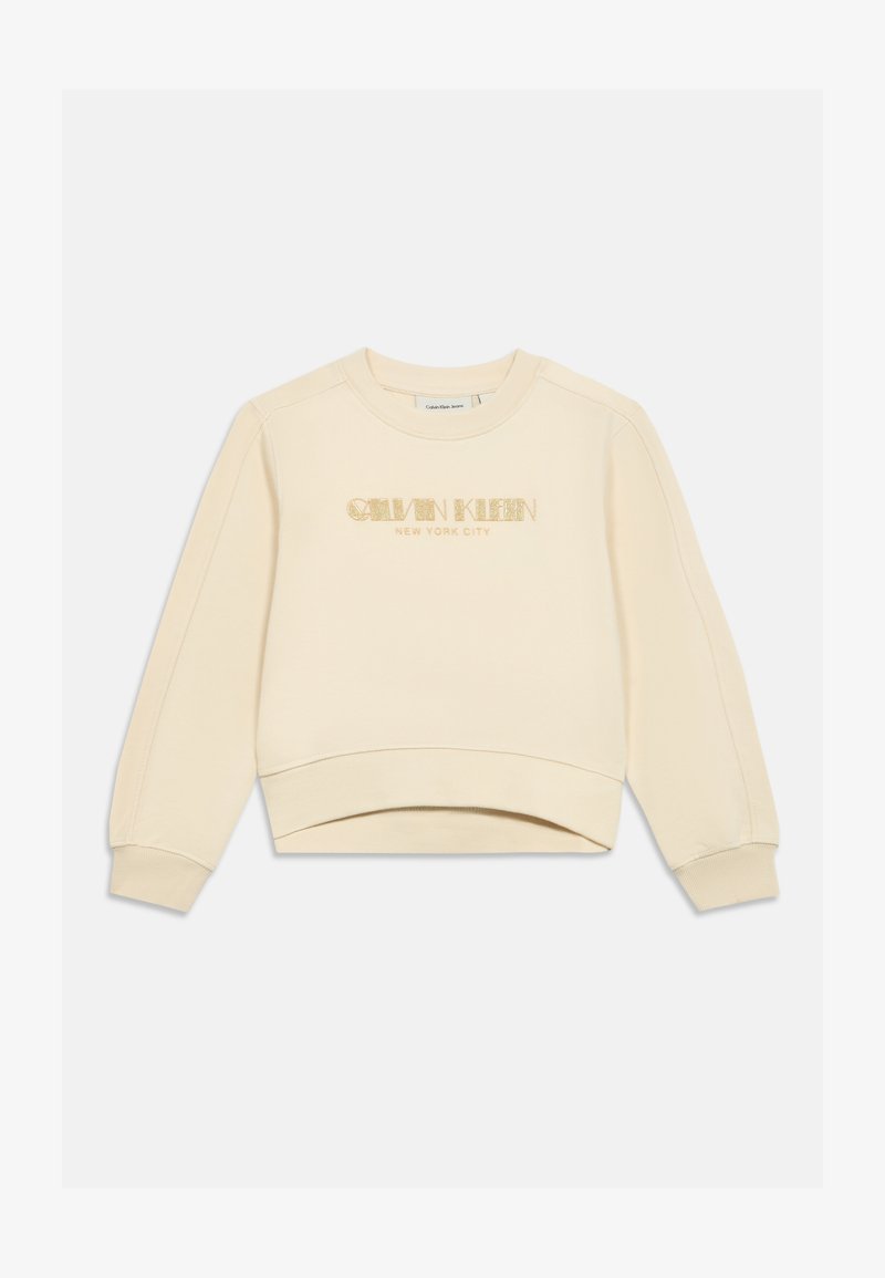 Felpa color crema realizzata in tessuto morbido. Presenta un collo rotondo, spalle basse e un logo luccicante "Calvin Klein NEW YORK CITY".