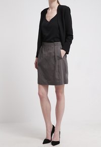 Haut noir à col en V, blazer noir ajusté sur une jupe gris mi-longue avec des plis à l'avant, porté avec des escarpins noirs à bout pointu, textures de tissu lisse.