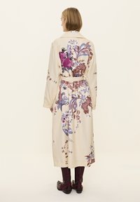 Kremasti cvjetni bathrobe s dugim rukavima, na leđima s ljubičastim i ružičastim cvjetovima. Uključuje odgovarajući pojas i pada ispod koljena.