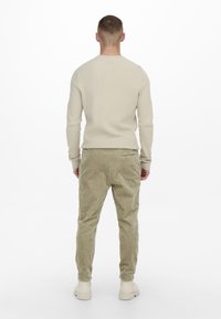Suéter de canalé beige combinado con pantalones de pana verde oliva. Botas gruesas de color claro. Textura de tela suave con costuras visibles.