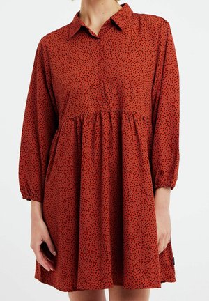 Robe couleur rouille avec un col, des boutons à l'avant et des manches longues. Présente une taille froncée et un motif à pois noirs sur l'ensemble.