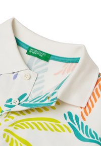 Camisa polo de tejido blanco, con patrones de hojas coloridos en verde, azul, naranja y púrpura. Con cuello, botones y una etiqueta verde.