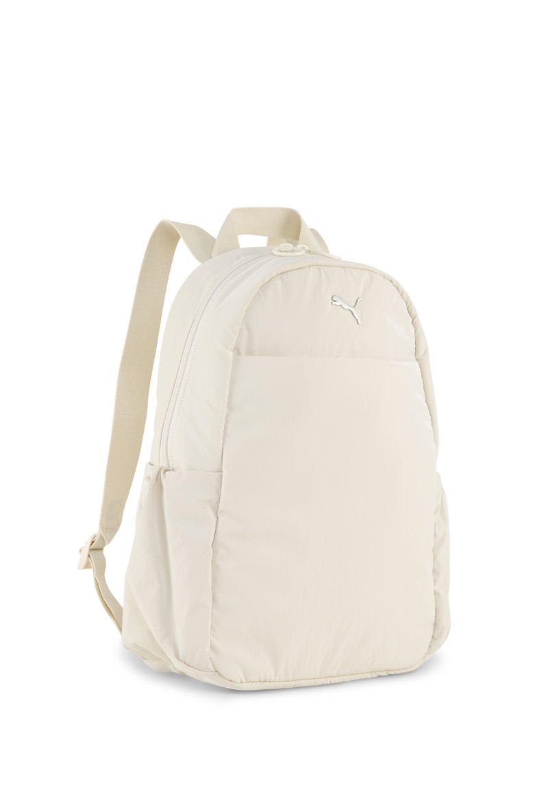 Mochila de color beige claro, hecha de un material suave y acolchado. Forma redondeada, con un bolsillo frontal con cremallera y correas ajustables. Logo en la parte frontal.