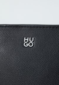 Portofel din piele neagră, cu o suprafață texturată și un accent cu logo-ul argintiu "HUGO". Design compact cu un finisaj neted pe margine.