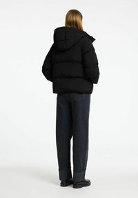Sort puffervindjakke med hætte, quiltet design og brede ærmer, parret med mørk denimbukser og sorte ankelstøvler.