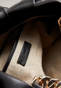 Intérieur d'un sac en cuir noir avec une doublure en tissu beige, une petite étiquette en cuir noir et un accent de chaîne dorée.