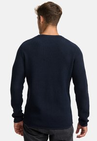 Maglione lavorato a maglia blu marino con trama testurizzata, maniche lunghe e colletto girocollo. Dettagli di cucitura visibili nei polsini e sull'orlo.