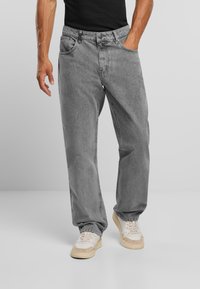 Jeans di denim grigio con vestibilità comoda, cinque tasche e sottili dettagli di cucitura, abbinati a sneakers color crema e beige.