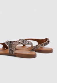 Sandalias planas marrones con un diseño de estampado de serpiente en negro y beige. Cuentan con una cinta ancha y un acento de hebilla plateada. Textura de cuero suave.
