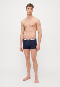 Nachtblaues Baumwoll-Boxershorts mit einem weißen und roten Moschino-Logo-Bund, die eine enge Passform und eine glatte Textur aufweisen.
