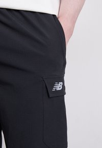 Sorte cargo shorts med en sidelomme med knaplukning og et hvidt New Balance-logo. Fremstillet af et let, struktureret stof.