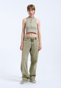 Top corto de color verde claro con cuello alto, combinado con jeans de corte holgado en verde claro y zapatillas grises. Textura suave con detalles mínimos.
