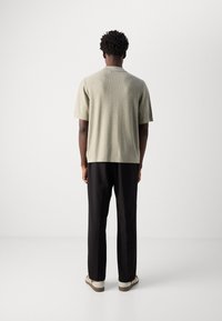 Khaki geribd shirt met korte mouwen en een ronde hals, gedragen met zwarte broek en witte sneakers met bruine accenten.