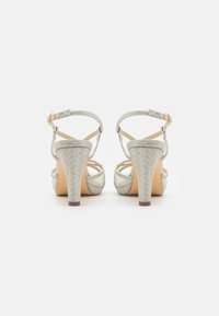 Heeled sandals in silver fabric with a woven pattern, open back, adjustable ankle strap, and a medium block heel.