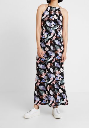 Robe maxi en tissu noir avec un col halter, ornée d'un motif floral vibrant en rose, bleu et vert. Assortie à des baskets blanches.