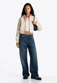 Cremefarvet cropped bomberjakke over en rødstribet skjorte med knapper, parret med brede mørkeblå jeans. Accessoriseret med en marineblå taske.