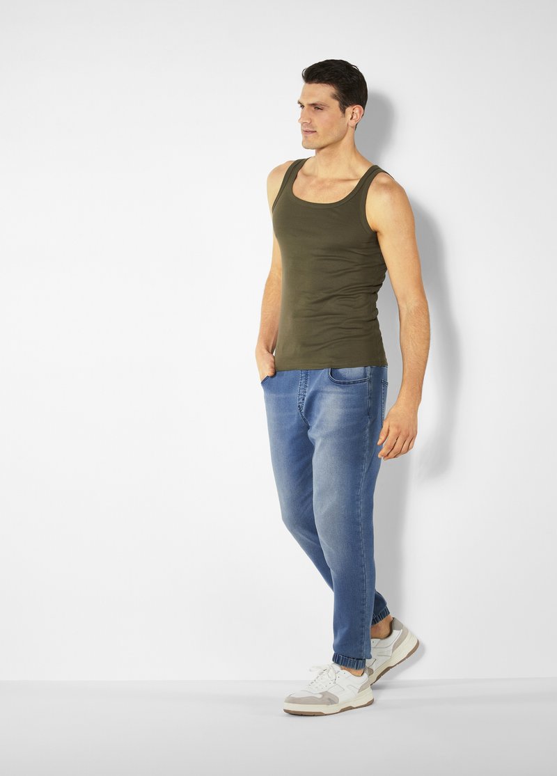 Olive green tank top, casual blue jeans, and white sneakers with gray accents. Slim fit design, soft fabric, and simple silhouette.