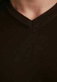 Ciemnobrązowy sweter w serek z prążkowanym dekoltem, gładką fakturą i dopasowanym krojem. Materiał wydaje się miękki i lekki.