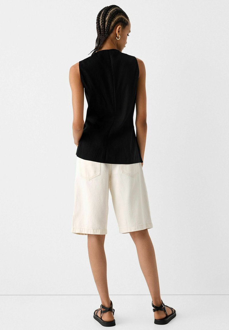 Czarny top bez rękawów o teksturowanym wykończeniu, w połączeniu z kremowymi szortami dżinsowymi z tylnymi kieszeniami i luźnym krojem.