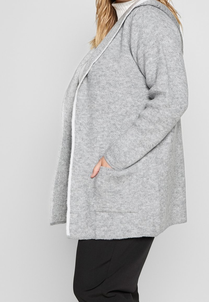 Cardigan grigio lavorato a maglia con cappuccio, caratterizzato da una finitura testurizzata, apertura frontale e tasche laterali. Il design è rilassato e non strutturato.