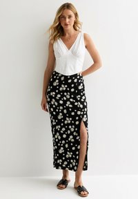 Black floral maxi skirt with white daisy pattern, featuring a side slit. Paired with a white fitted top and black sandals.
