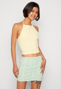 Top halter amarelo com costura texturizada, combinado com uma mini saia floral verde-clara com um design ajustado e cintura elástica.