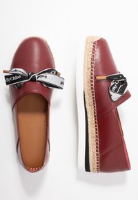 Ballerines en cuir bordeaux avec une semelle blanche, finition en jute et accents en ruban noir. Texture lisse et design à bout rond.