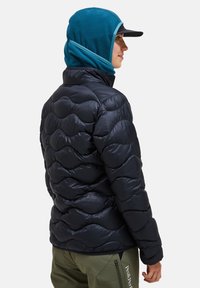 Navy kleurige pufferjack met een geborduurd ontwerp, gecombineerd met een teal fleece kap. De persoon draagt olijfgroene broek met een ritszak.