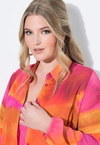 Blusa dai colori vivaci con una sfumatura di rosa e arancione, design con bottoni e polsini arricciati con dettagli a motivo.
