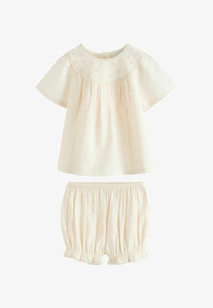Costum pentru bebeluși de culoarea cremei, cu bluză cu mâneci scurte având broderie florală și pantaloni scurți cu talie elastică, cu tivuri cu volănașe.