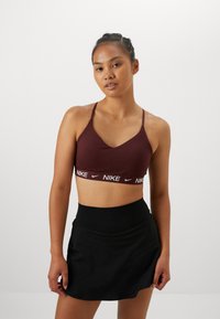 Nike sportmelltartó, bordó színben, vékony pántokkal, fehér márkázott szalaggal. Pántos tőle egy fekete, testhezálló szoknya, sima textúrával, sportos dizájnnal.