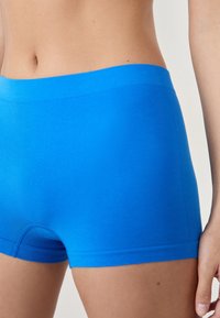 Boxers en coton bleu avec une texture lisse, une taille large et une coupe ajustée. Présente un détail de couture décoratif à l'ourlet.