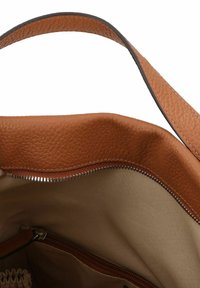 Interior de bolsa tote de cuero marrón claro con un bolsillo con cremallera, forro liso en beige y detalles en el borde de textura marrón. Diseño de parte superior abierta visible.
