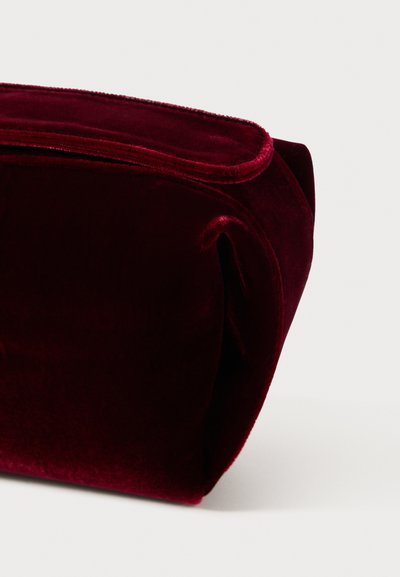 Vinrød fløjl kosmetikpose med en glat tekstur, rektangulær form og rullede kanter, der har en subtil glans. Ingen hardware eller accenter synlige.