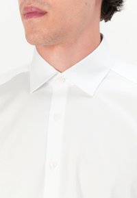 Weißes Hemd mit Button-Down-Kragen, glatter Textur und einer Frontleiste mit drei Knöpfen. Einfaches Design ohne Muster.
