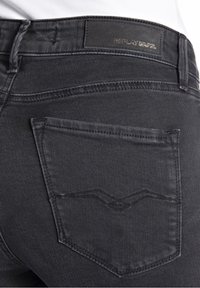 Primer plano del bolsillo trasero de unos vaqueros de mezclilla negros con un diseño de costura sutil y una etiqueta de marca de cuero negro en la cinturilla.