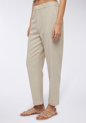 Pantaloni beige su misura con una texture liscia, gamba affusolata e tasche laterali. Abbinati a sandali piatti con cinturini di un colore chiaro.