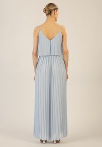 Vestido maxi plisado de color azul claro con dobladillo en capas y tirantes finos. Diseño en la parte posterior en V y textura suave. Llevado con tacones beige.