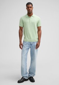 Jasnozielona koszulka polo z krótkim rękawem i żebrowanym kołnierzykiem, w połączeniu z wyblakłymi niebieskimi dżinsami prostymi i czarnymi butami. Prosty design, swobodny wygląd.